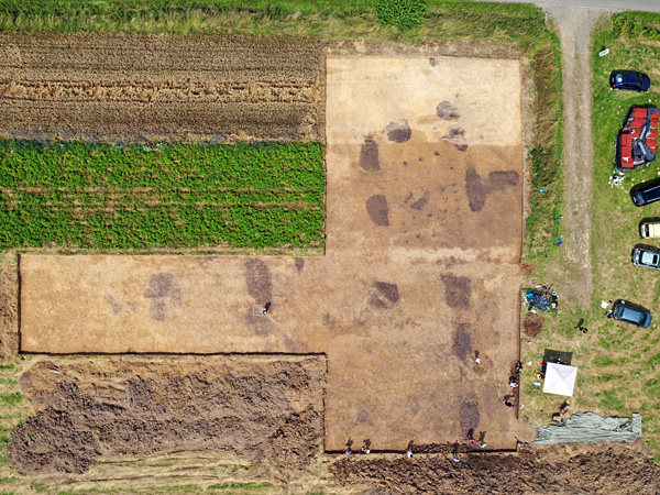 Aerial view of the T-shaped excavations. On one side are strips of cultivated fields, on the other are parked cars