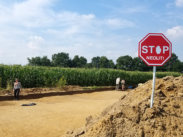 Rectangular surface devoid of topsoil. In front, a red sign driven into a pile of earth with the inscription: STOP, Neolithic